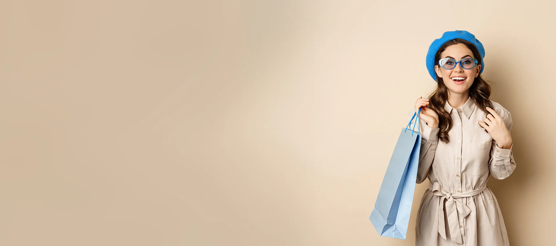 Woman in a trench coat and blue beret holding a shopping bag against a beige background